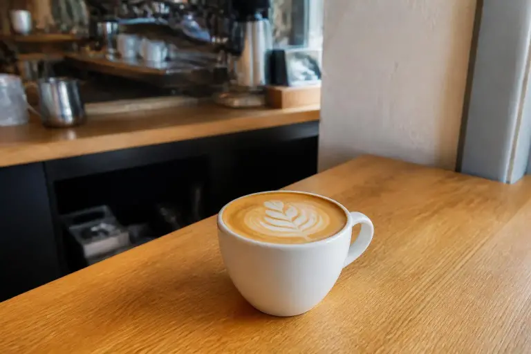 Latte avec un dessin de feuille dans une tasse blanche, sur le comptoir en bois d'un coffee shop